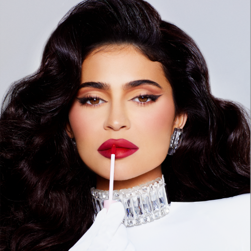 Kylie Jenner models against a red lipstick by Kylie Cosmetics, while wearing a white outfit with crystal detailing