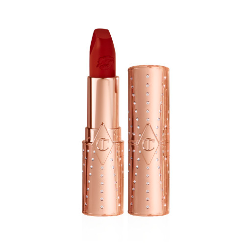 A packshot of the CHARLOTTE TILBURY Matte Revolution Coronation Red. The product is cut out against a white background. The case is rose gold, studded with crystals. The lipstick bullet is a deep crimson red.