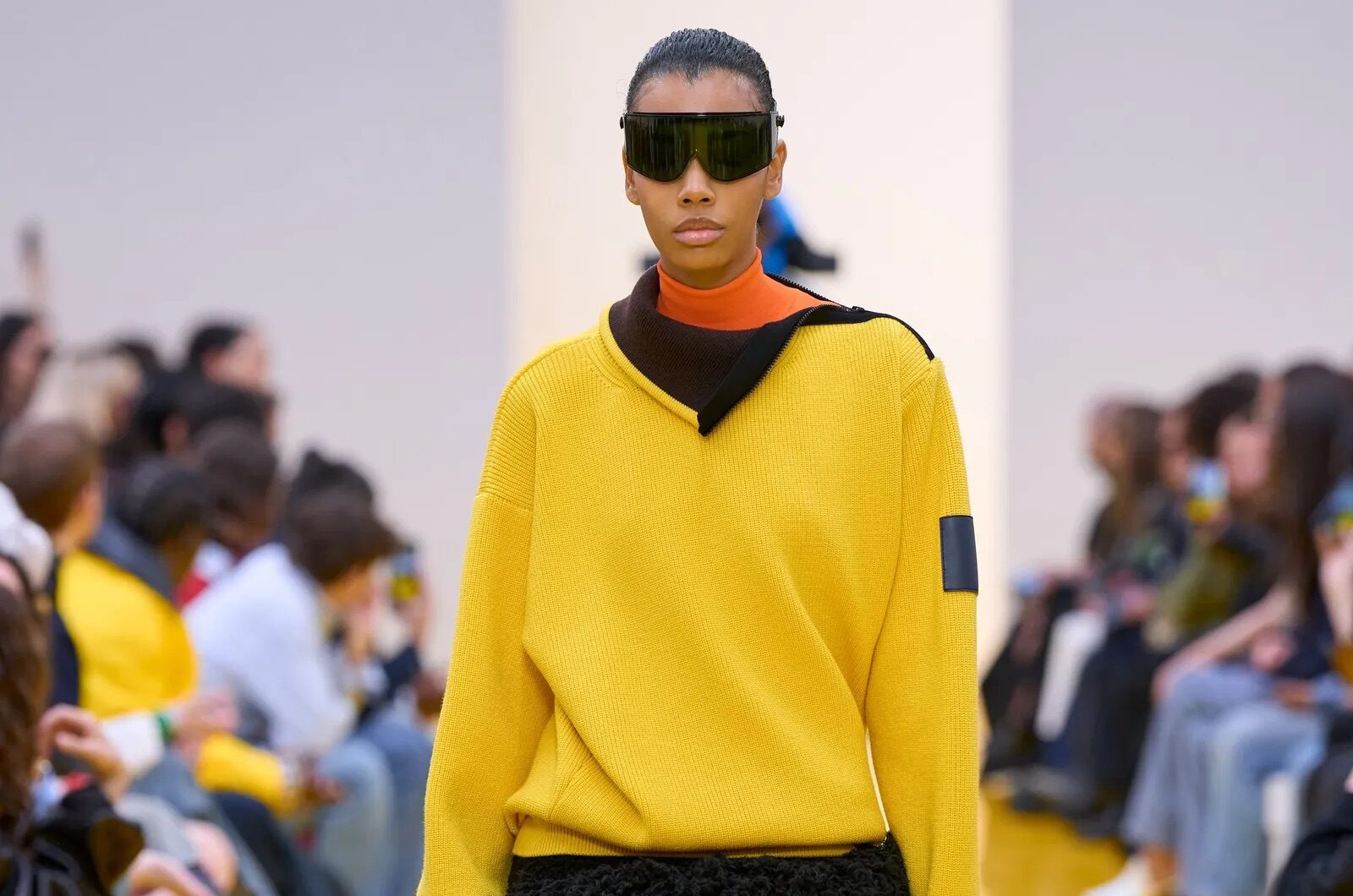 Modelo en pasarela con suéter amarillo y falda rizada negra.