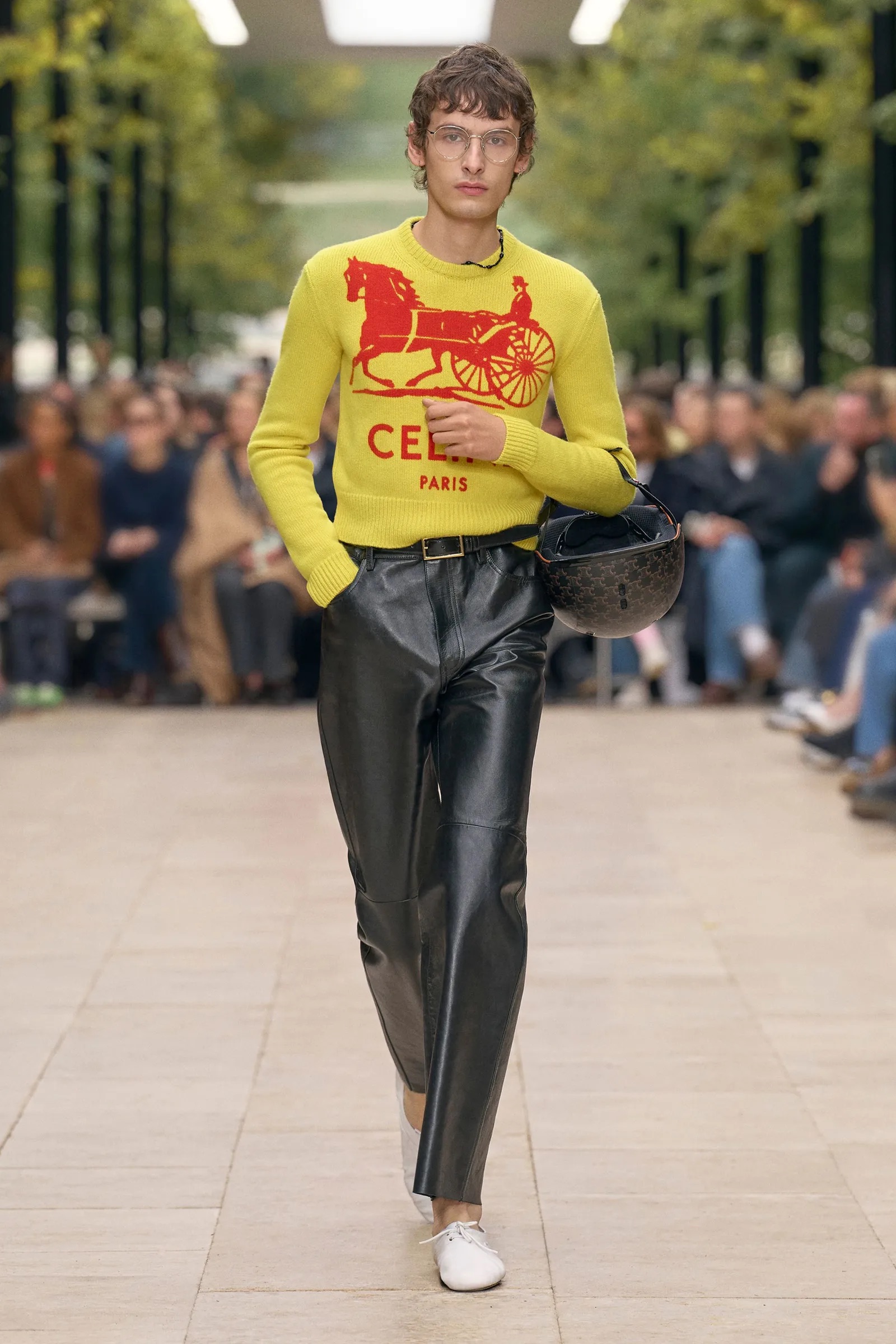 Modelo masculino con suéter amarillo gráfico de Celine y pantalones de cuero.