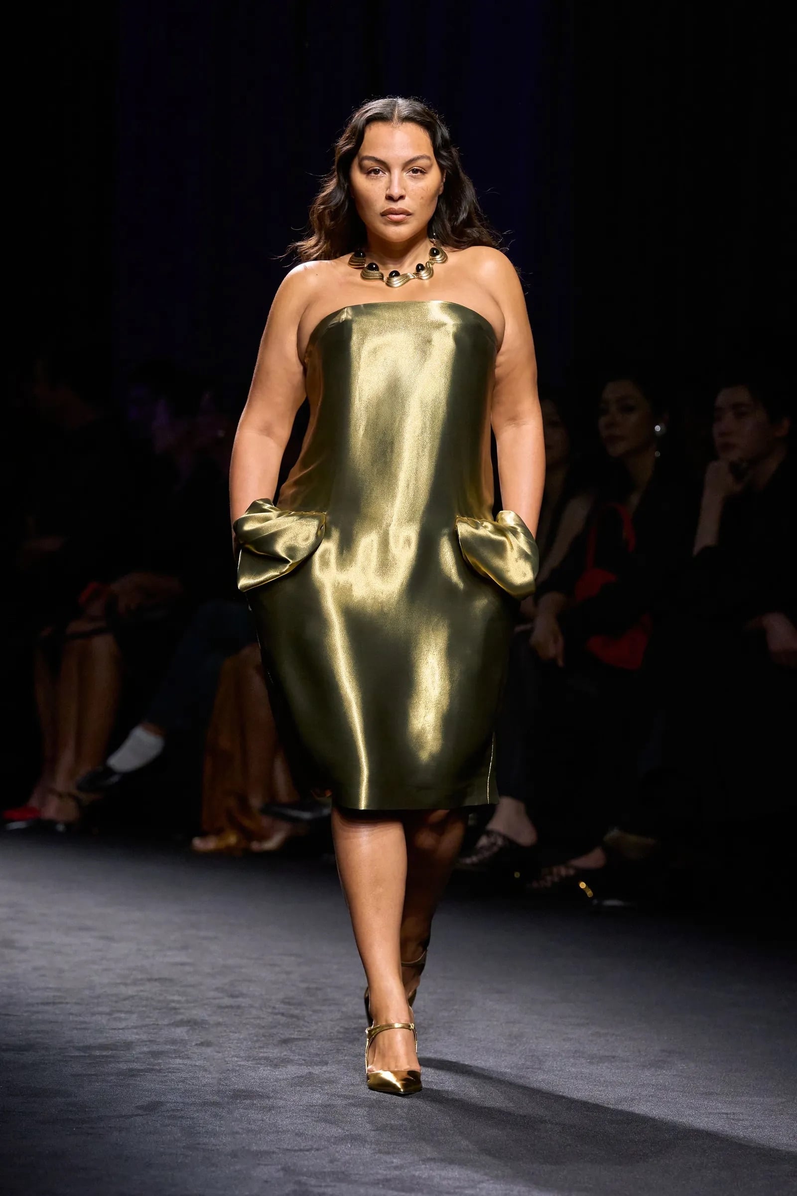 Modelo luciendo un vestido midi metálico en tono dorado con silueta estructurada y bolsillos laterales abullonados a la altura de la cadera