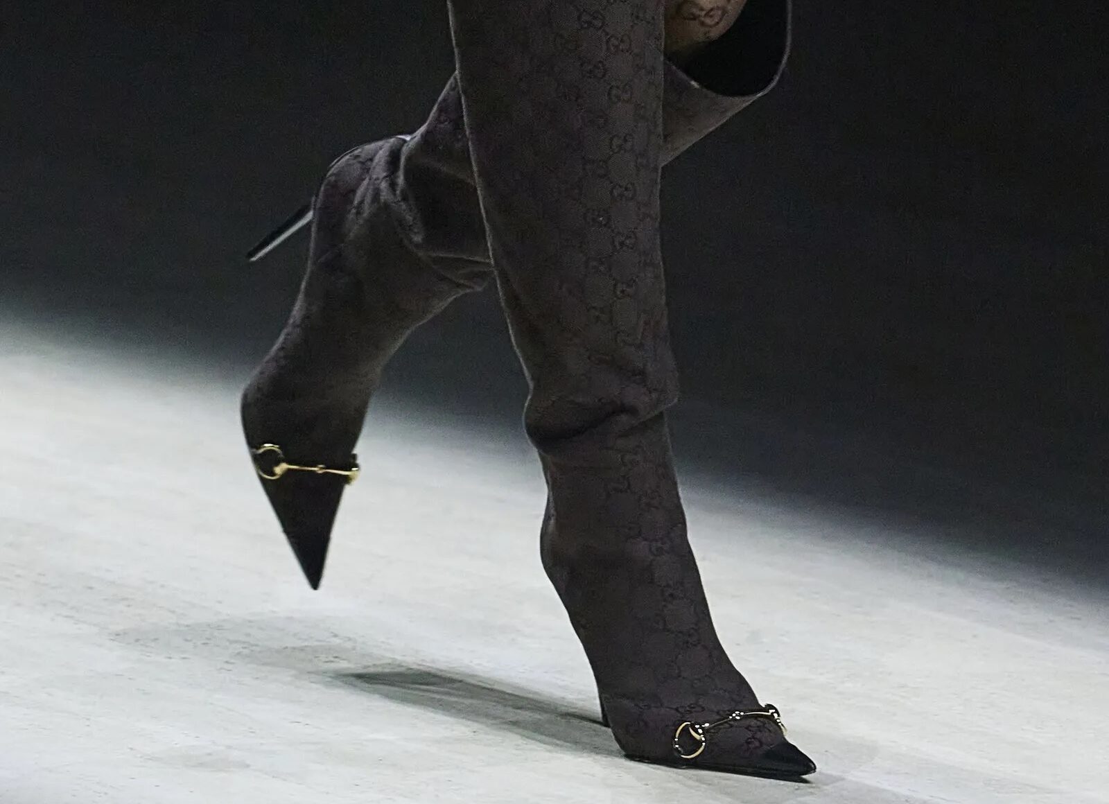 Botas altas oscuras con monograma de Gucci y detalle metálico en la punta.