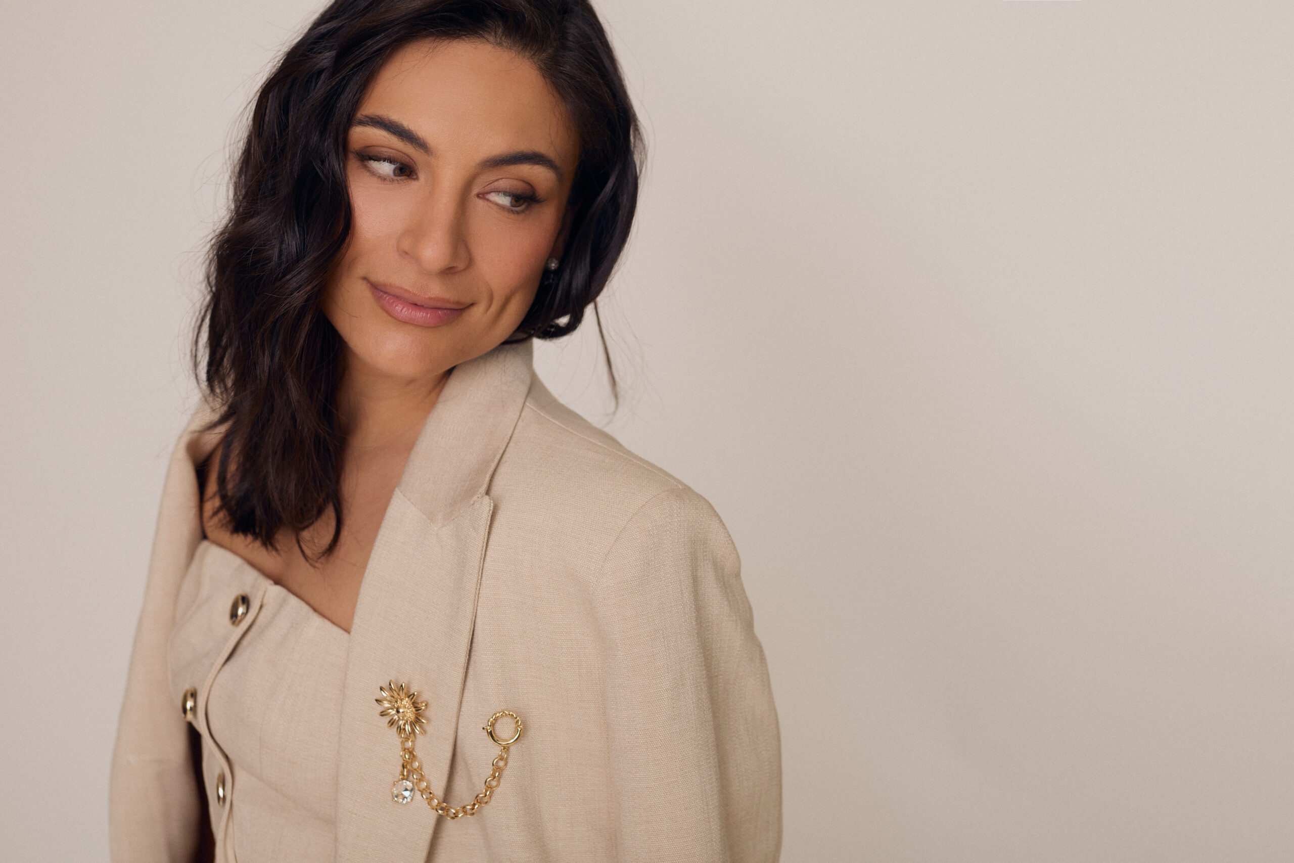 Retrato de perfil de Ana Brenda Contreras con la mirada hacia un lado, vistiendo un conjunto sastre color beige con detalles de pedrería y un broche dorado en la solapa. Styling: JJ Rizo | Maquillaje: Kariana Martínez | Hair: Omar Álvarez