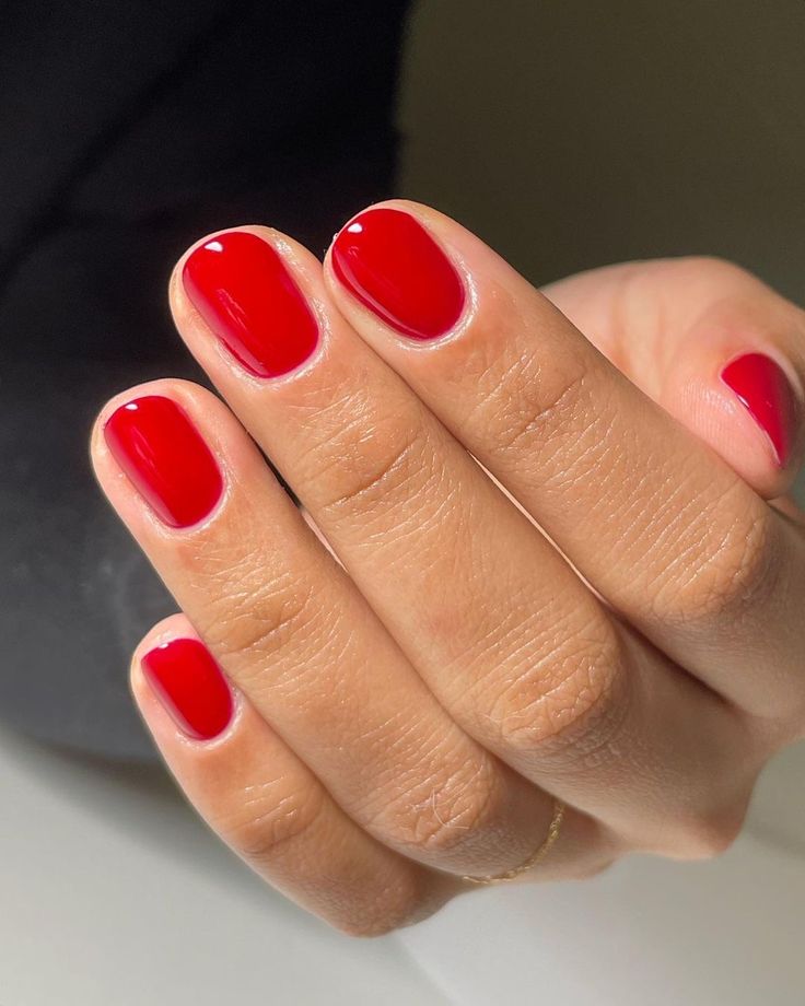 Mano con manicura corta y redondeada en un tono rojo brillante e intenso con acabado ultrabrillante.