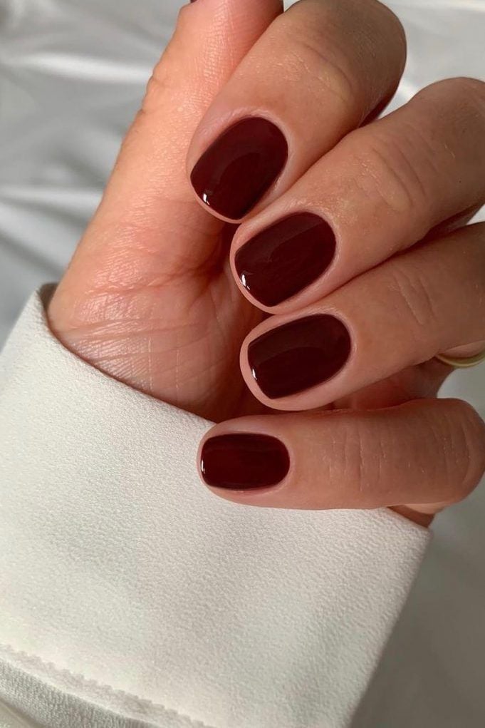 Mano con uñas cortas de forma cuadrada redondeada y un esmalte en tono burdeos oscuro con acabado brillante intenso.