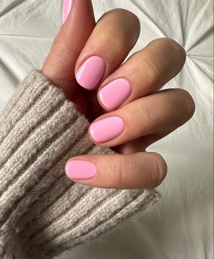 Mano con uñas cortas almendradas en tono rosa pastel sólido, posando sobre un suéter tejido de punto color beige.