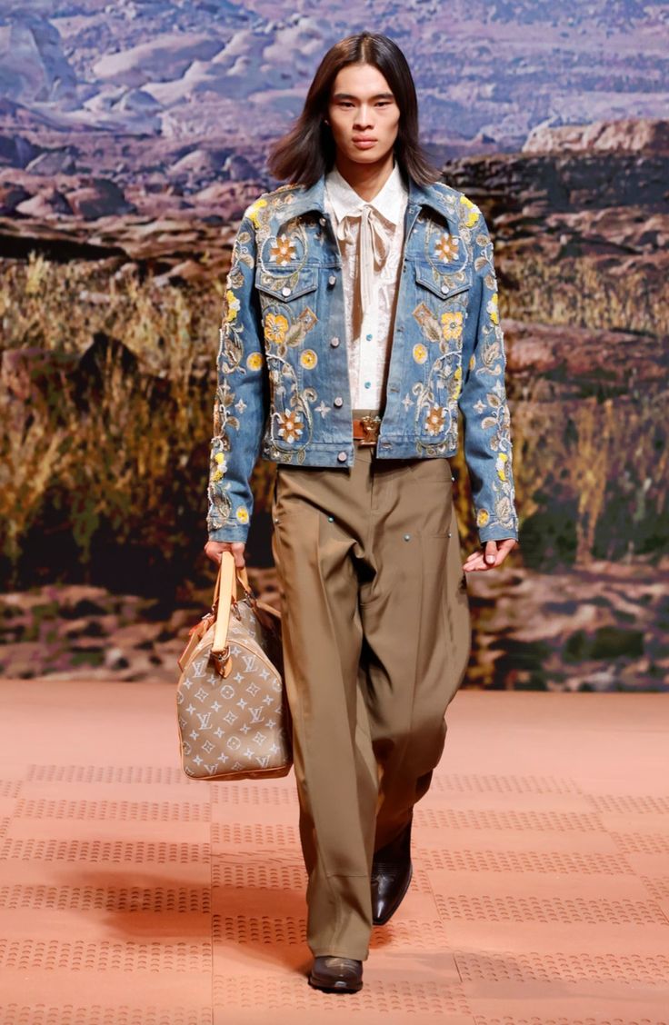 Modelo desfilando con una chaqueta de mezclilla azul clara con intrincados bordados florales en tonos amarillos y blancos.