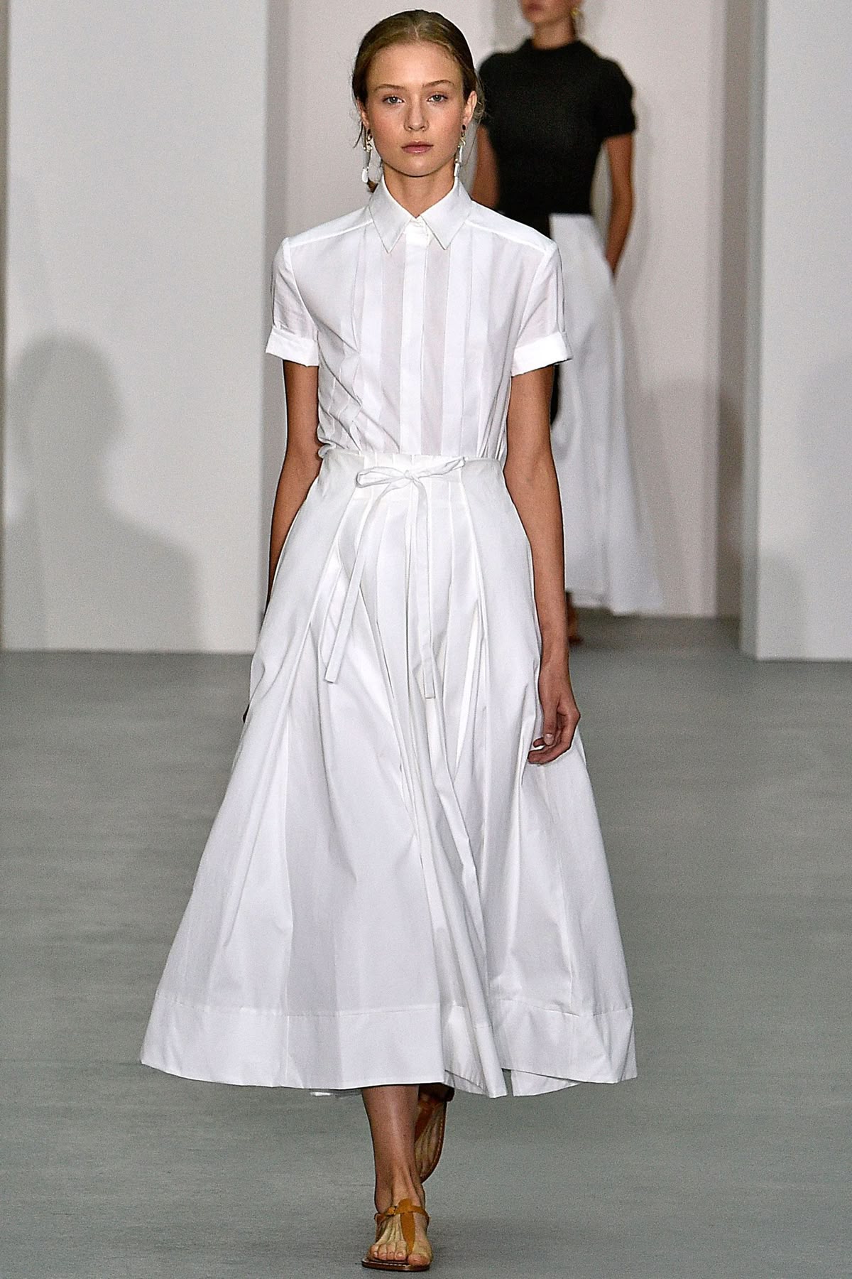 Modelo con vestido midi blanco de manga corta, fajín con lazo en la cintura y sandalias planas