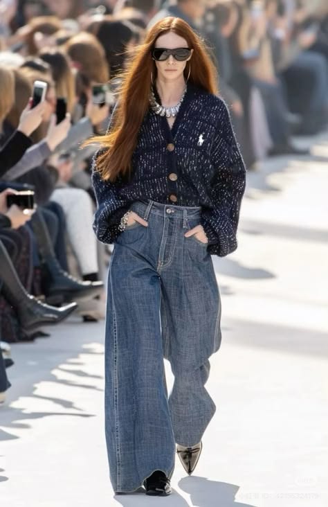 Modelo pelirroja luciendo un cárdigan de punto azul marino texturizado con botones, combinado con unos jeans anchos de mezclilla y gafas de sol en una pasarela