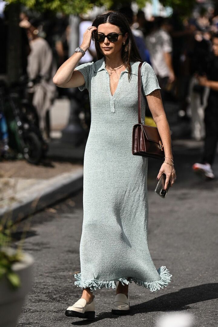 Mujer con vestido midi de punto celeste con cuello tipo polo, bajo con flecos, bolso marrón y mocasines claros