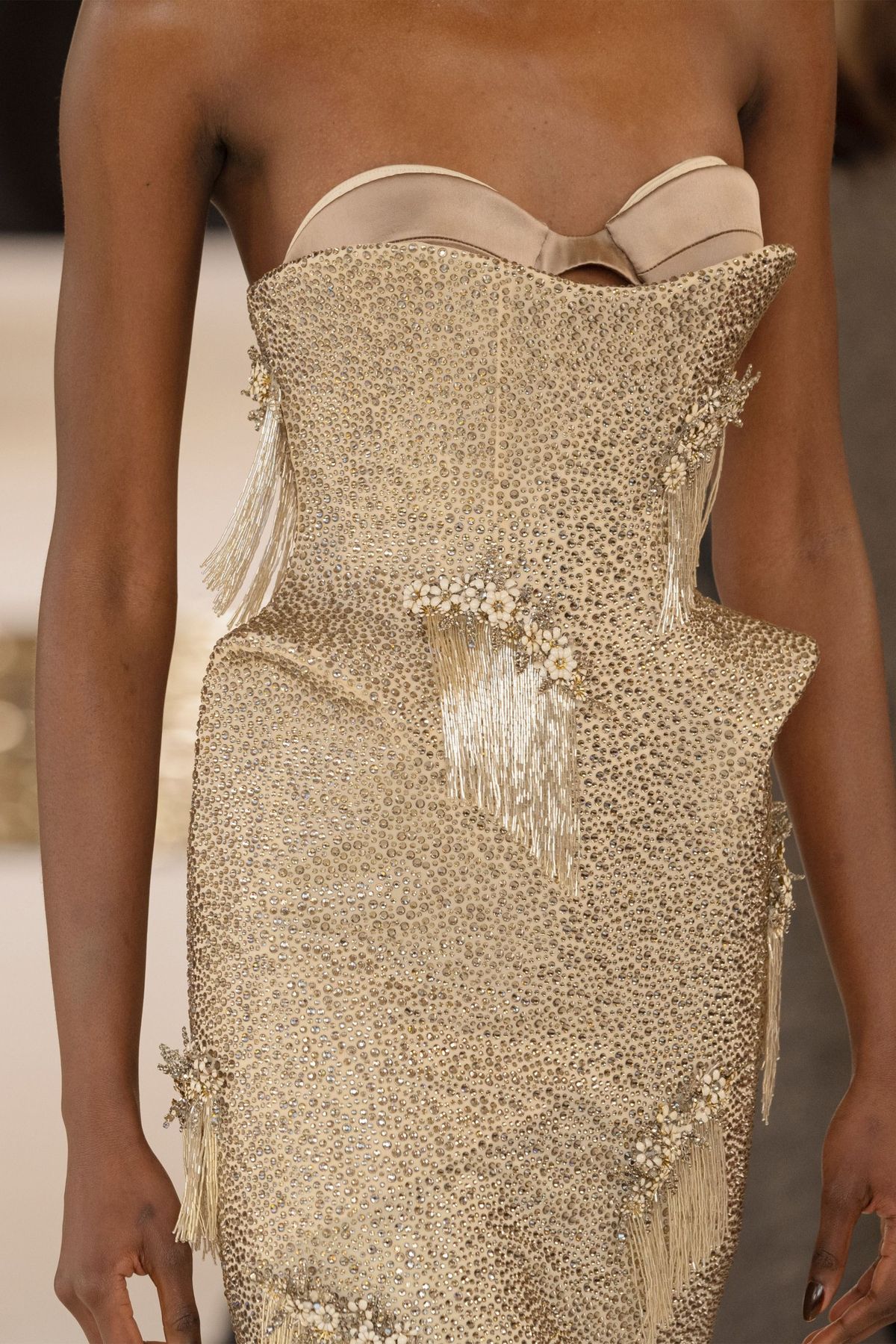 Detalle de un vestido strapless con incrustaciones de cristales, un corpiño ajustado y caderas realzadas mediante una estructura con vuelo y flecos colgantes.