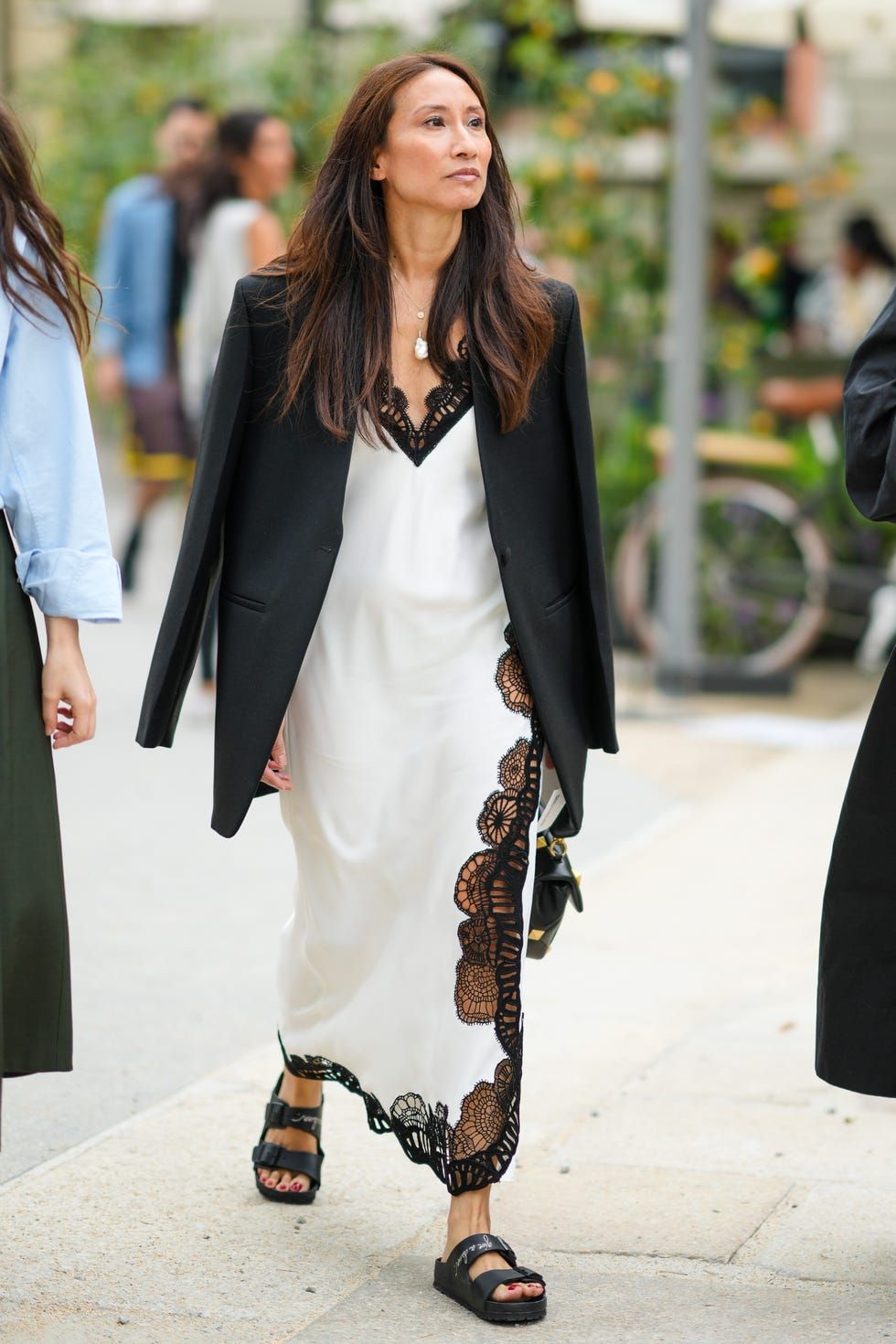 Mujer con vestido slip dress blanco de detalles negros de encaje y un blazer negro sobre los hombros
