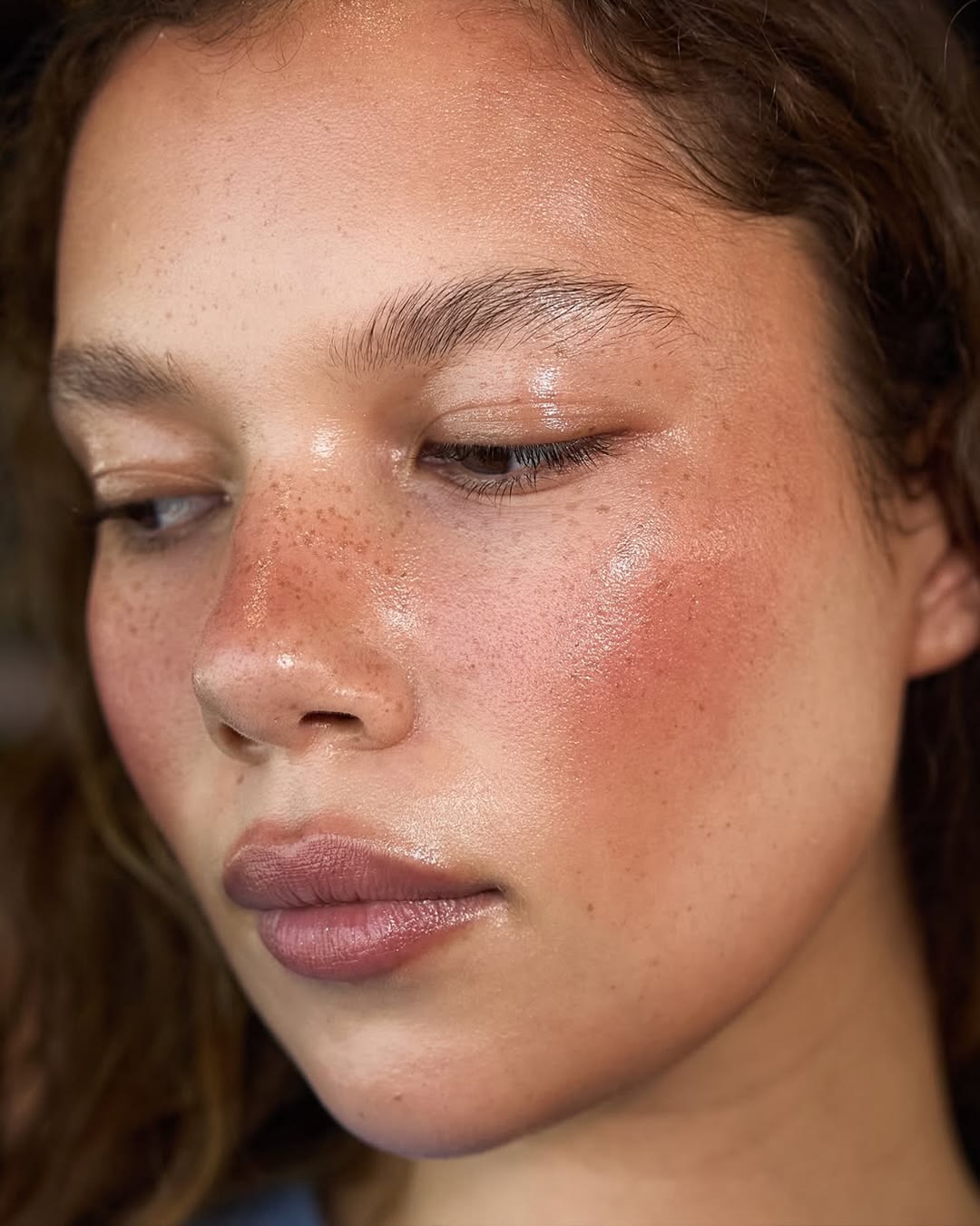 Primer plano de una modelo con rostro salpicado de pecas, piel luminosa con efecto brillante e hidratado, y mejillas sonrojadas