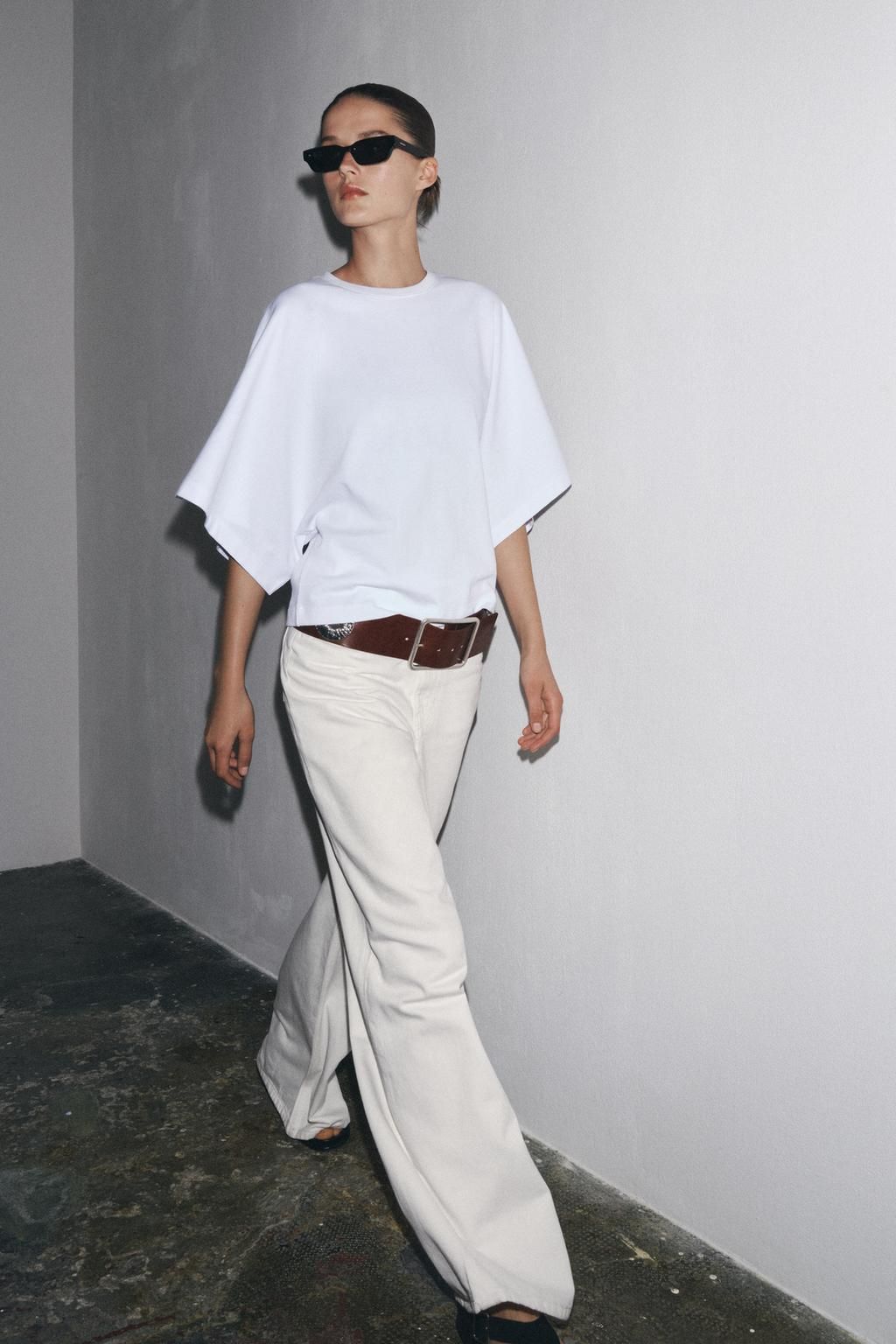 Modelo con camiseta blanca de mangas amplias, pantalones claros y un cinturón ancho marrón
