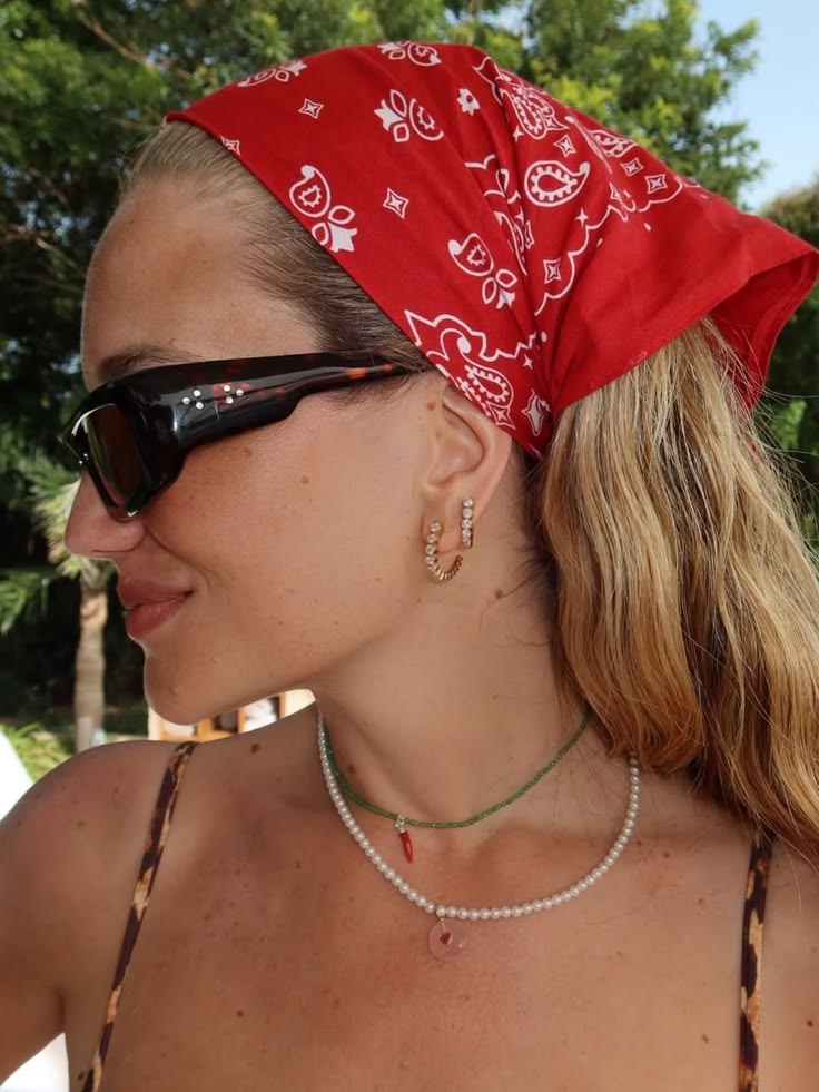Primer plano de una mujer con bandana roja Paisley, gafas de sol oscuras y collares superpuestos de perlas y cuentas verdes