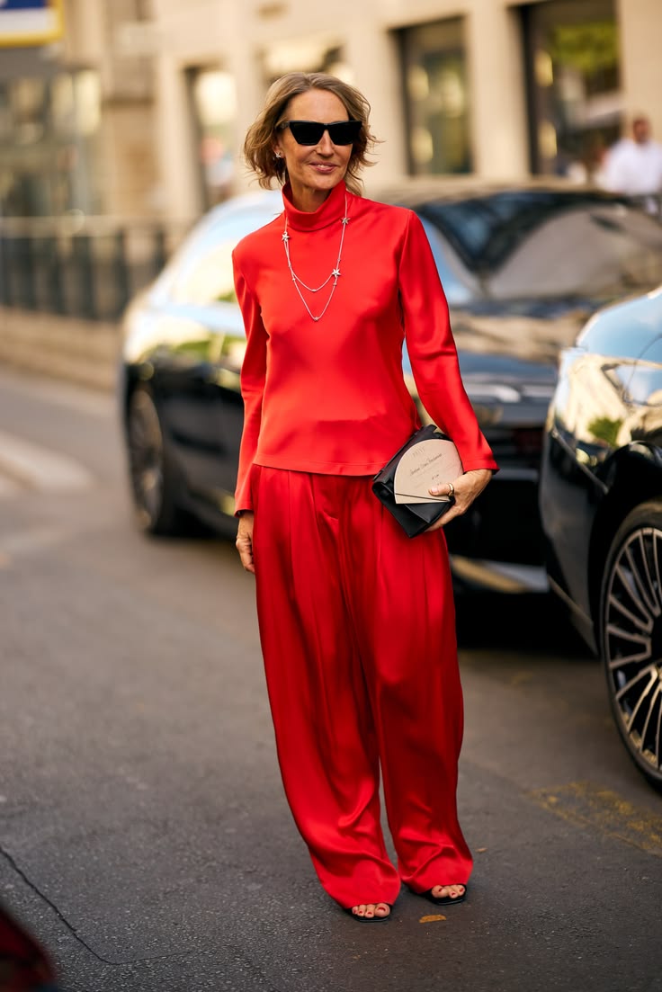 Mujer con conjunto rojo de cuello alto satinado, pantalones fluidos y un bolso de mano negro estructurado