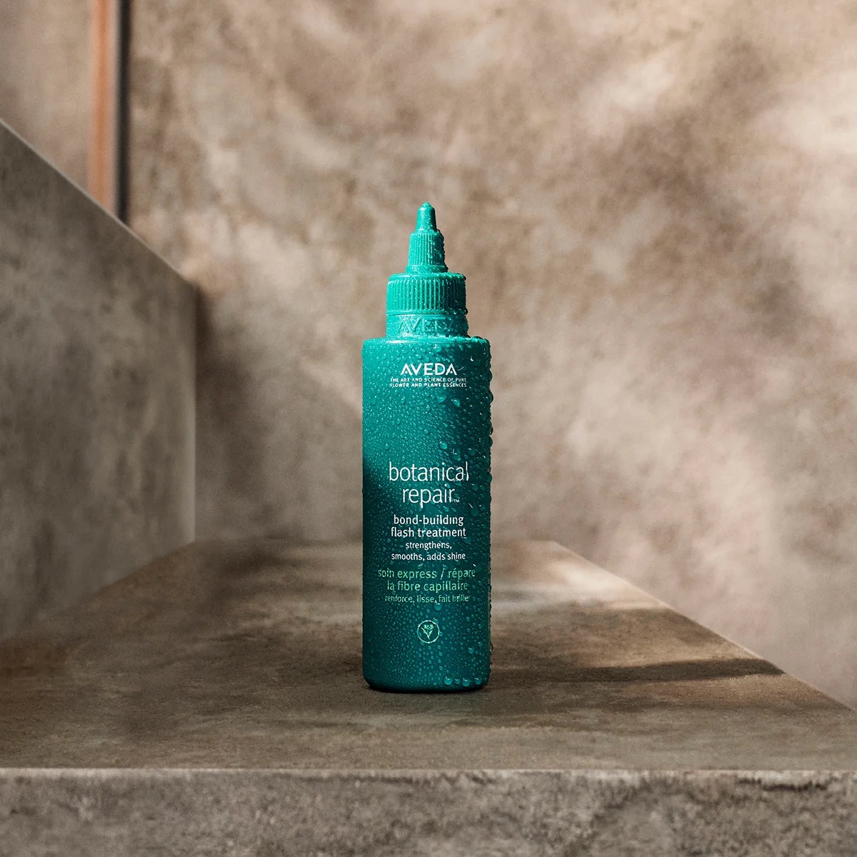 Botella de tratamiento capilar en gel "Botanical Repair Bond-Building Flash Treatment" de Aveda sobre una superficie de piedra rústica