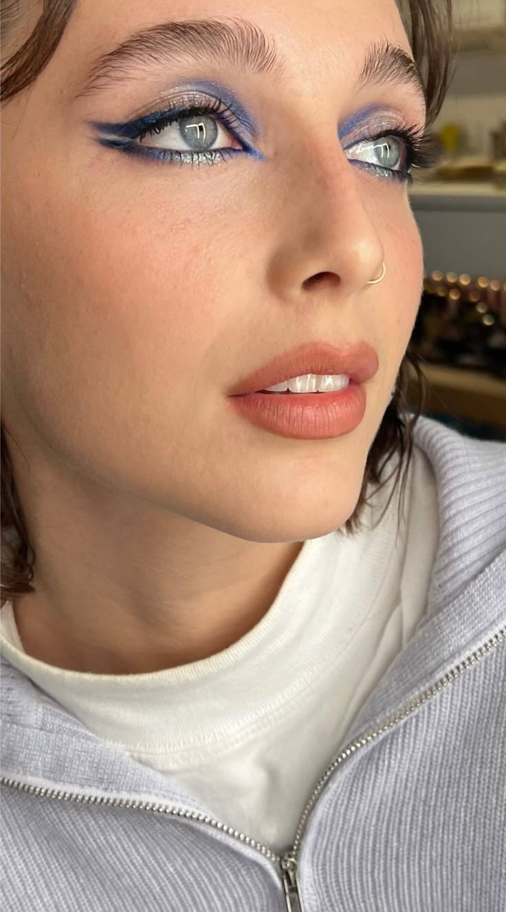 Primer plano de un rostro con ojos claros resaltados por un delineado gráfico azul y plateado brillante, acompañado de labios en tono nude cálido.