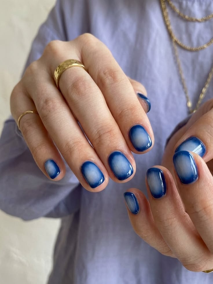 Manos luciendo uñas cortas cuadradas con un diseño degradado u ombré en tonos azul intenso con centro difuminado más claro.