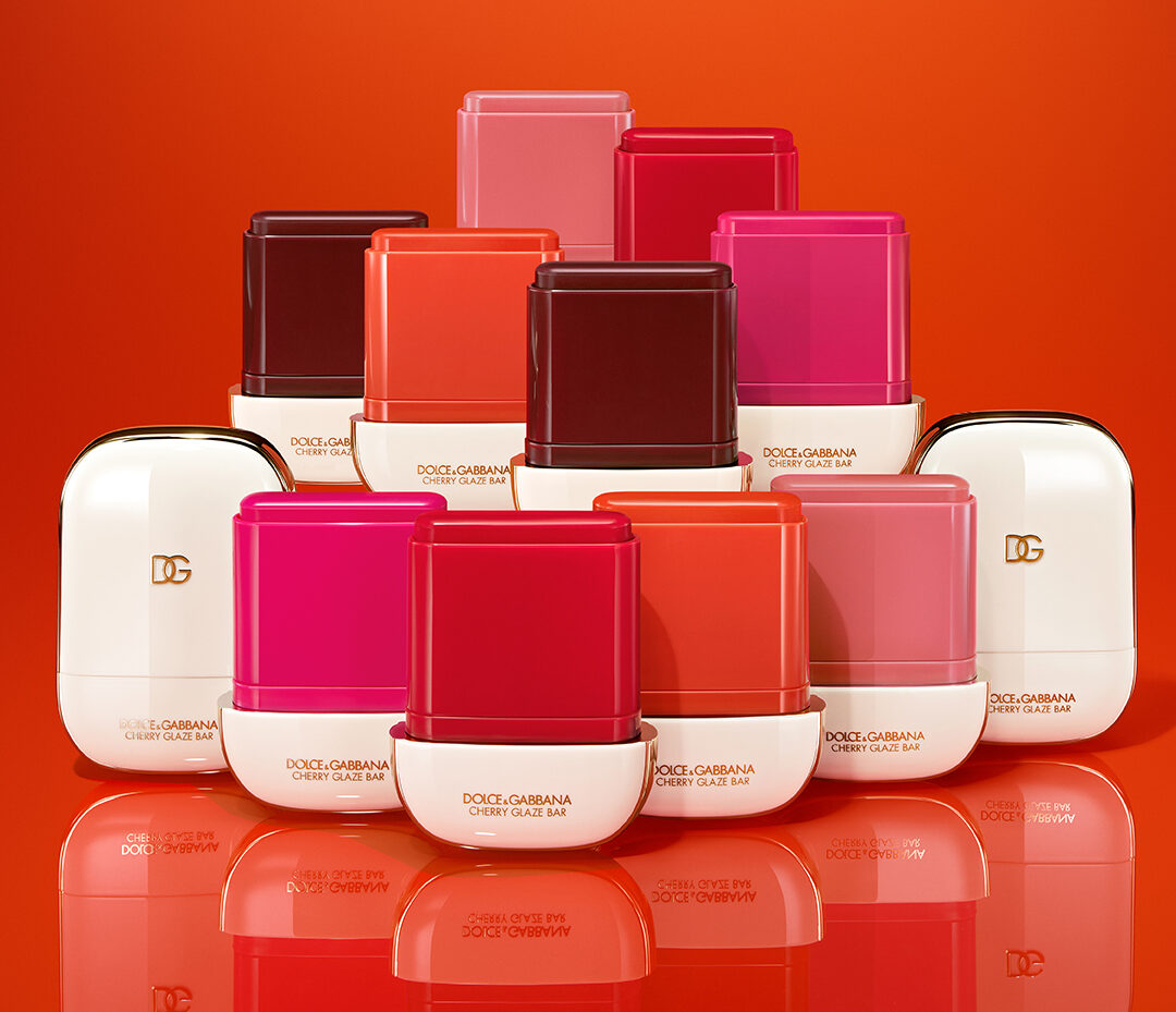 Composición de múltiples envases y barras abiertas de la colección Cherry Glaze Bar dispuestas en forma de pirámide sobre fondo naranja brillante.