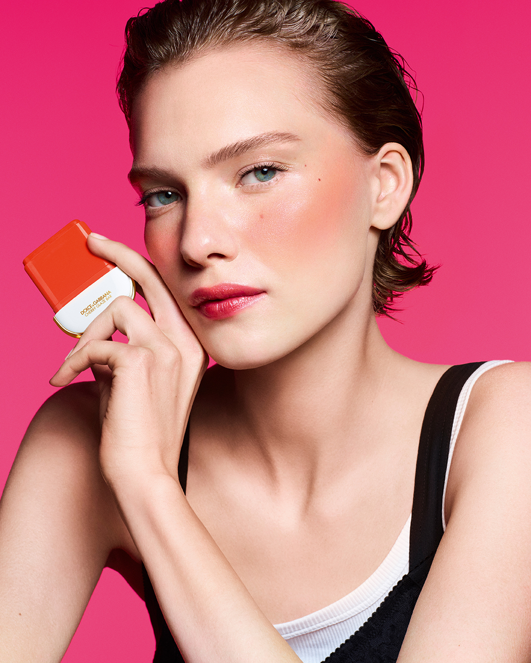 Modelo con cabello corto hacia atrás, mejillas con rubor rosado brillante y labios delineados, sosteniendo el aplicador de Cherry Glaze Bar.