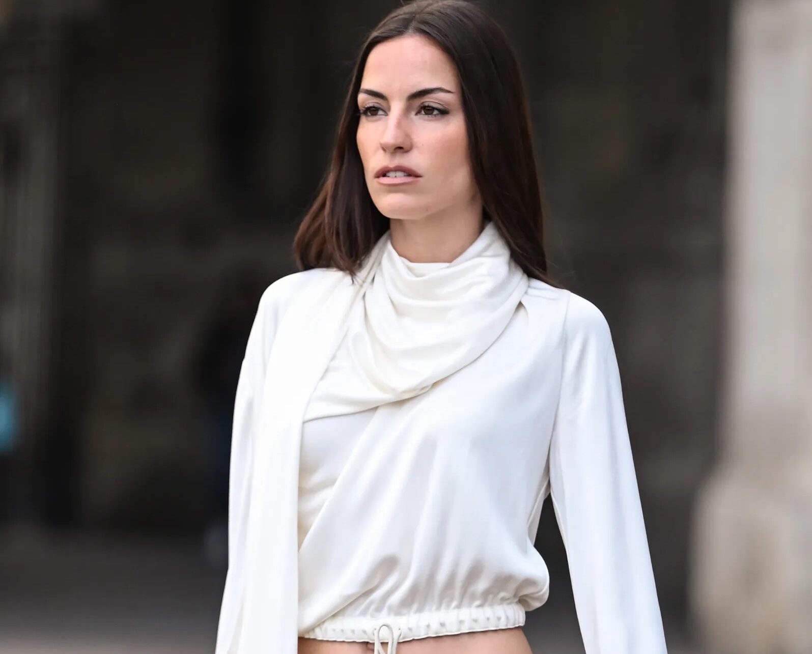 Modelo con blusa blanca fluida de cuello con pañuelo incorporado, cordón ajustable en la cintura, pantalones tipo cargo verde olivo y bolso borgoña.