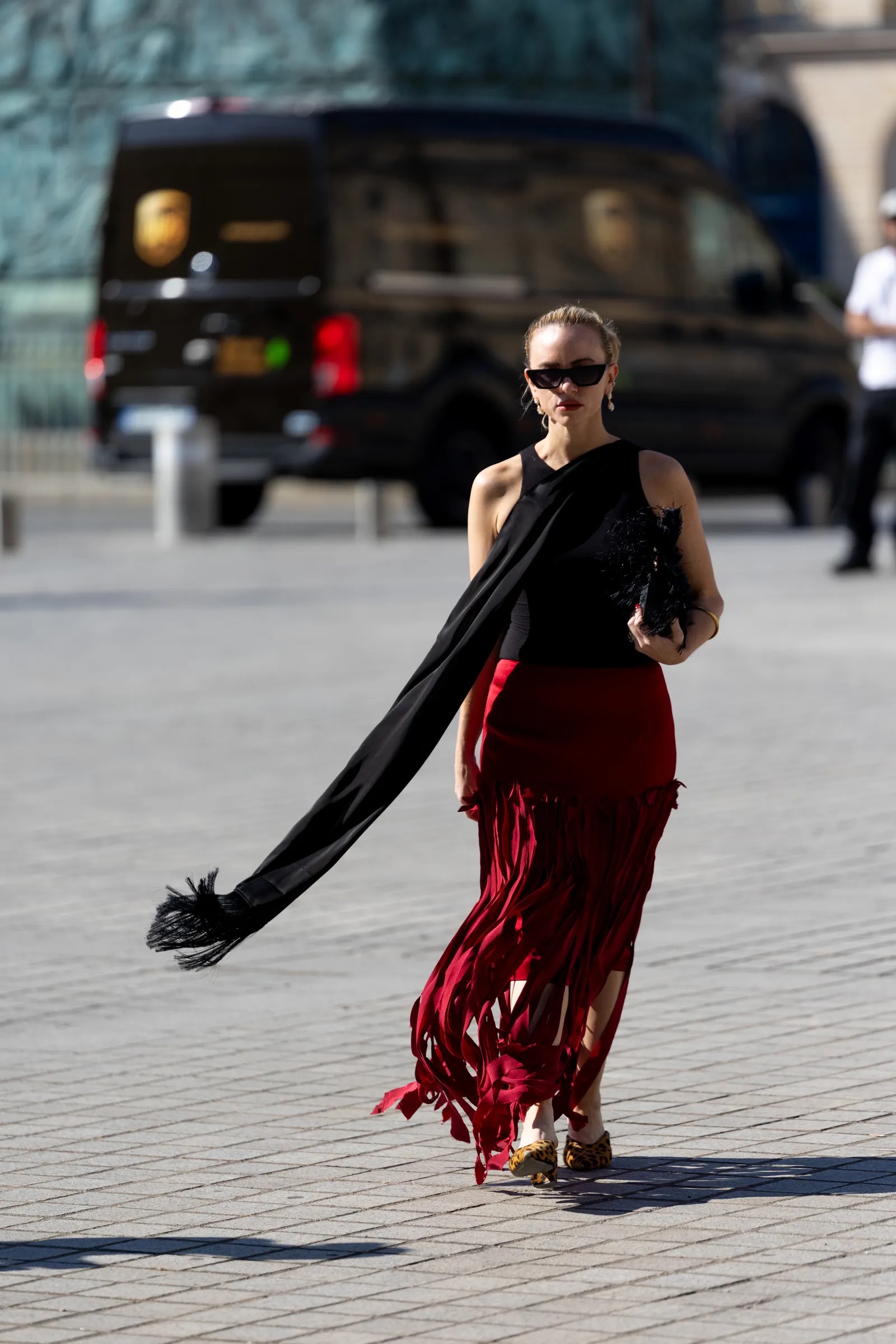 Mujer con top halter negro de tiras largas con flecos, falda roja larga con flecos y calzado de estampado animal.