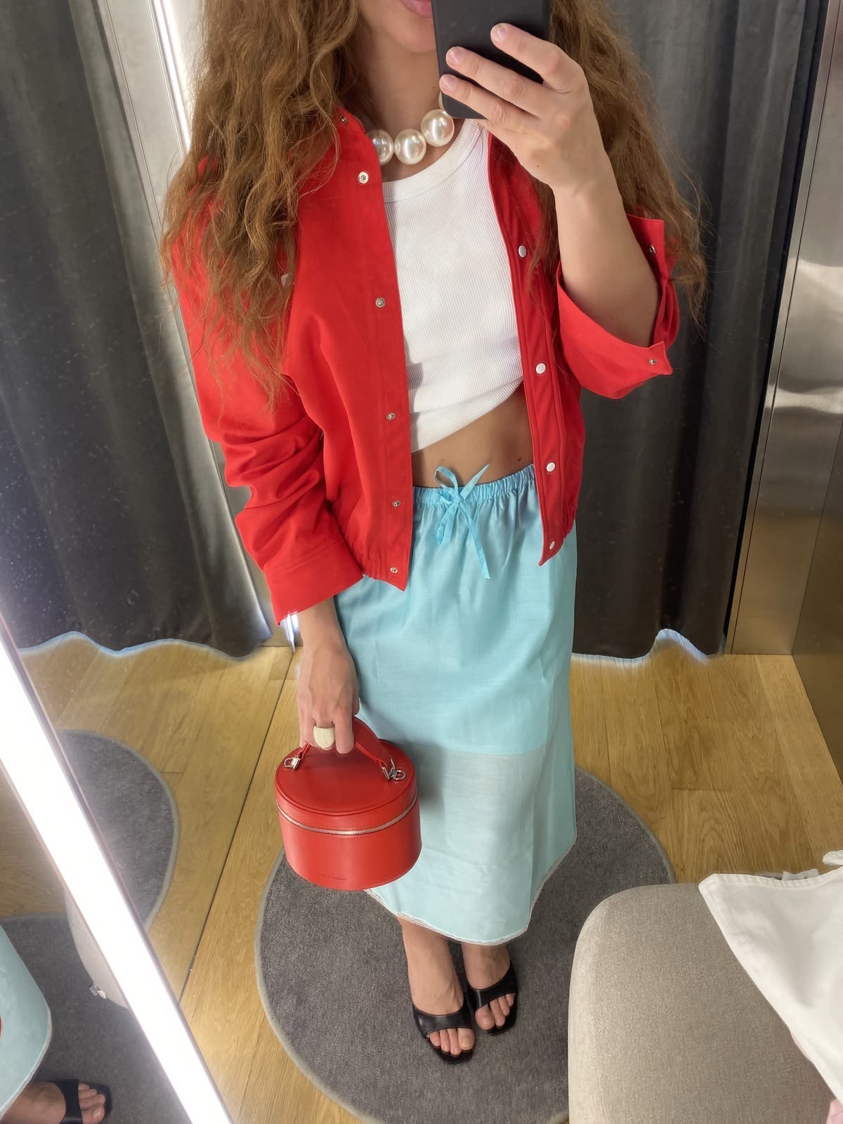 Mujer vestida con falda turquesa en combinación con suéter y bolso rojo