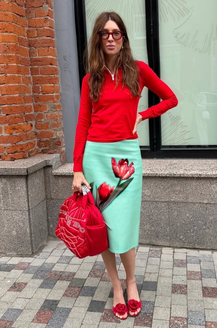 Mujer vestida con falda turquesa en combinación con suéter y bolso rojo