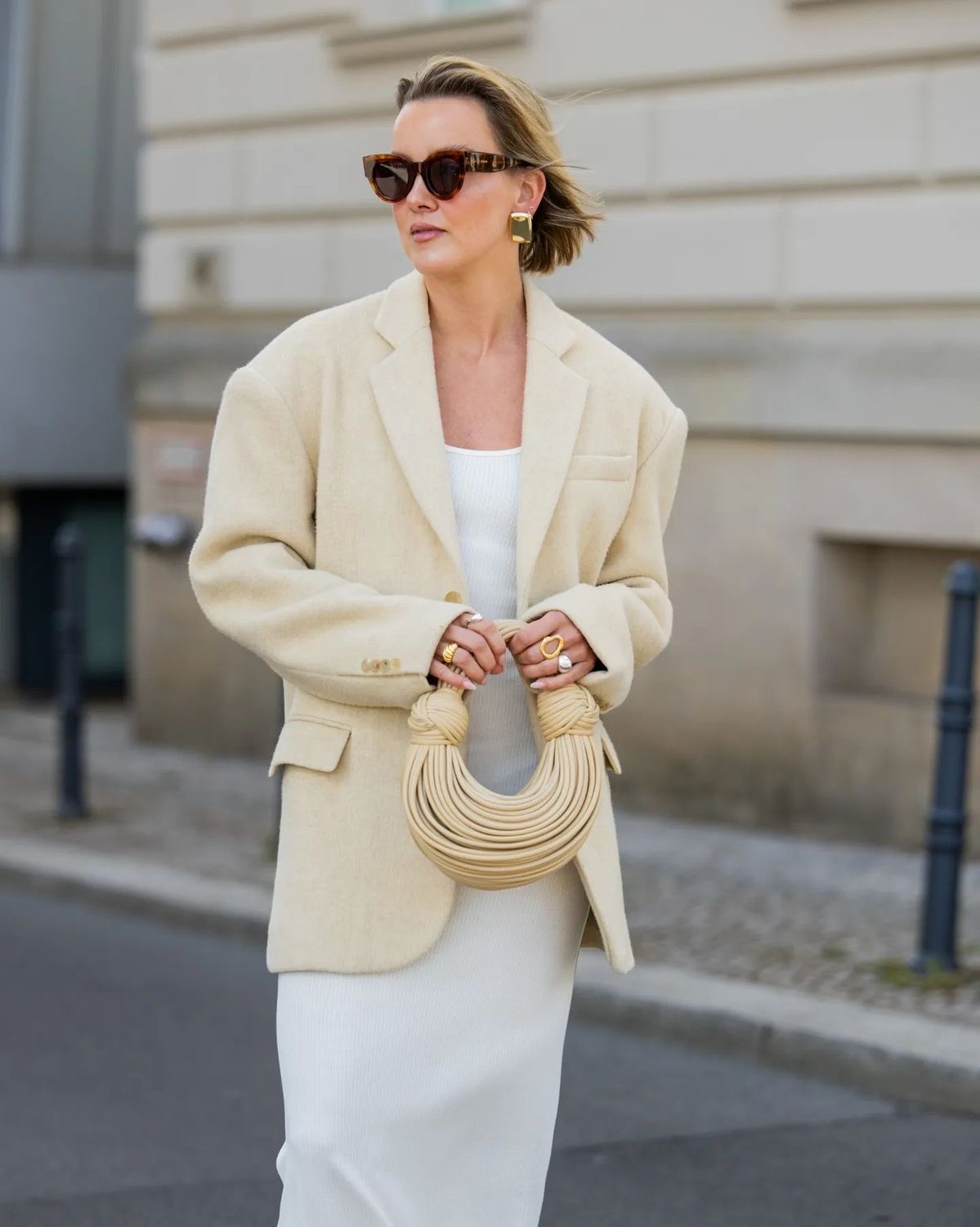 Mujer de lentes de sol con vestido blanco con blazer y bolso beige