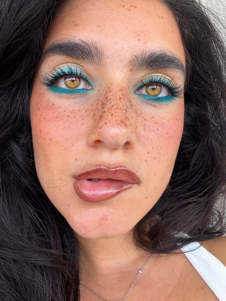 Rostro con abundantes pecas, cabello oscuro y una propuesta de maquillaje que combina sombras pastel con un delineado inferior en azul turquesa brillante.