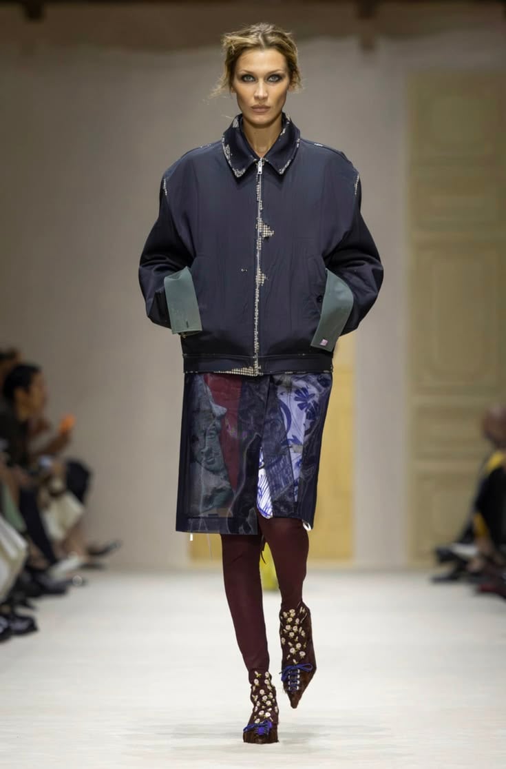 Modelo en pasarela con una cazadora bomber azul marino de cuello alto con detalles sutiles en los puños y la solapa.