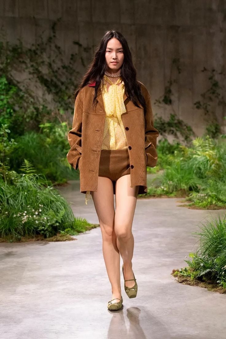 Modelo luciendo una chaqueta de ante marrón de corte recto y largo medio, combinada con shorts de punto y blusa estampada.