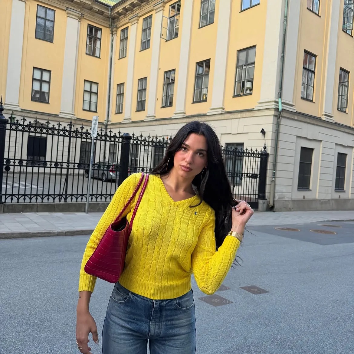 Dua Lipa con suéter amarillo trenzado y bolso rosa en la calle.