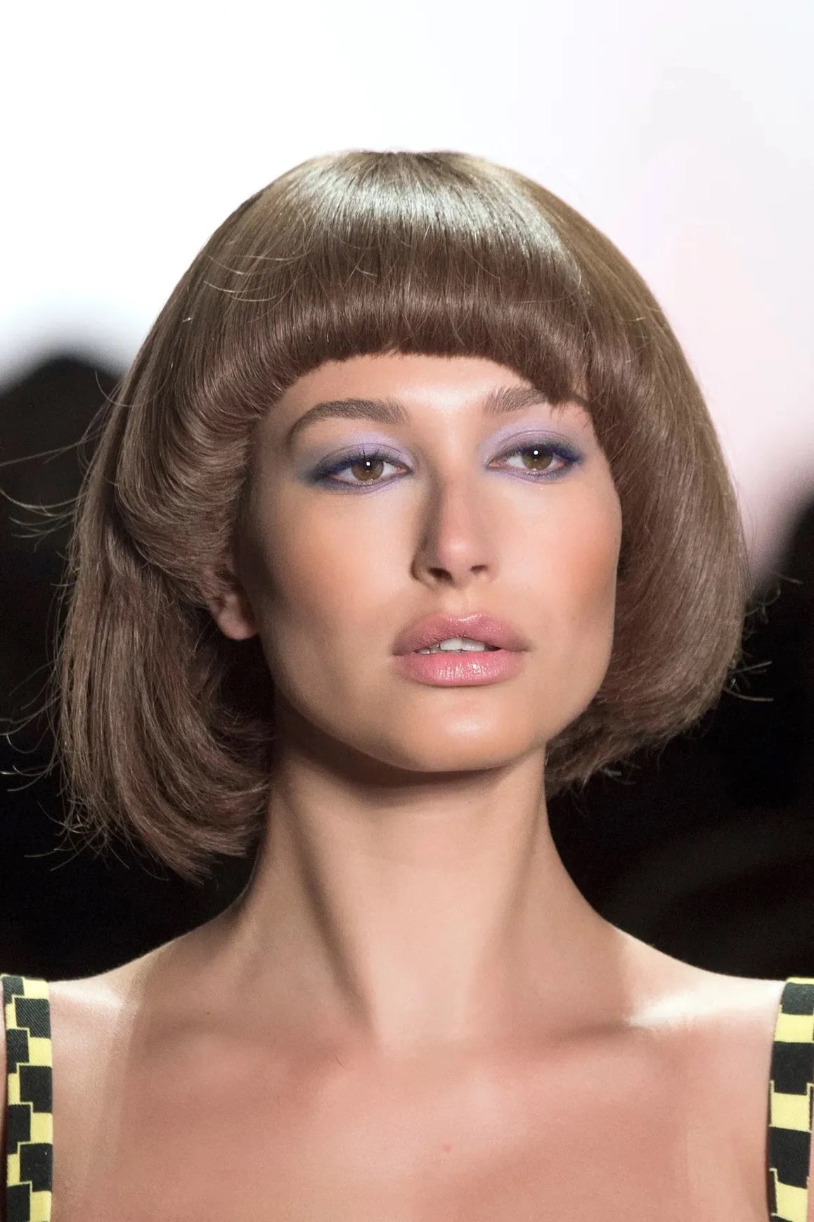Modelo con corte bob y flequillo recto, luciendo un maquillaje de ojos en tonos malva y morados suaves con labios nude rosados.