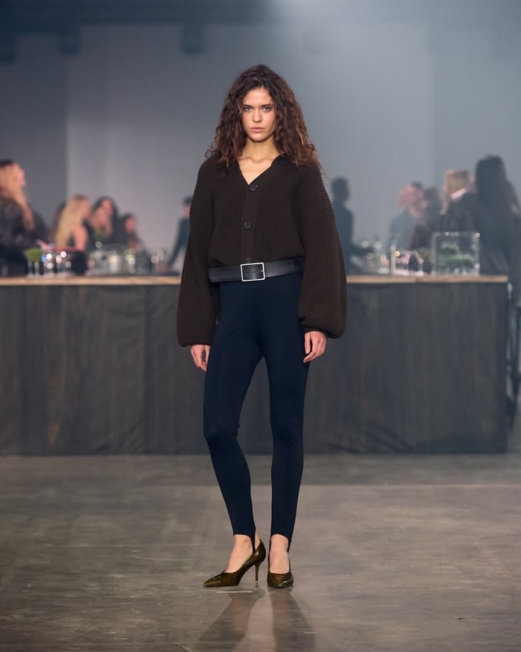 Modelo con suéter holgado de punto marrón y leggings con estribo en tono azul marino combinados con zapatos de tacón bajo.