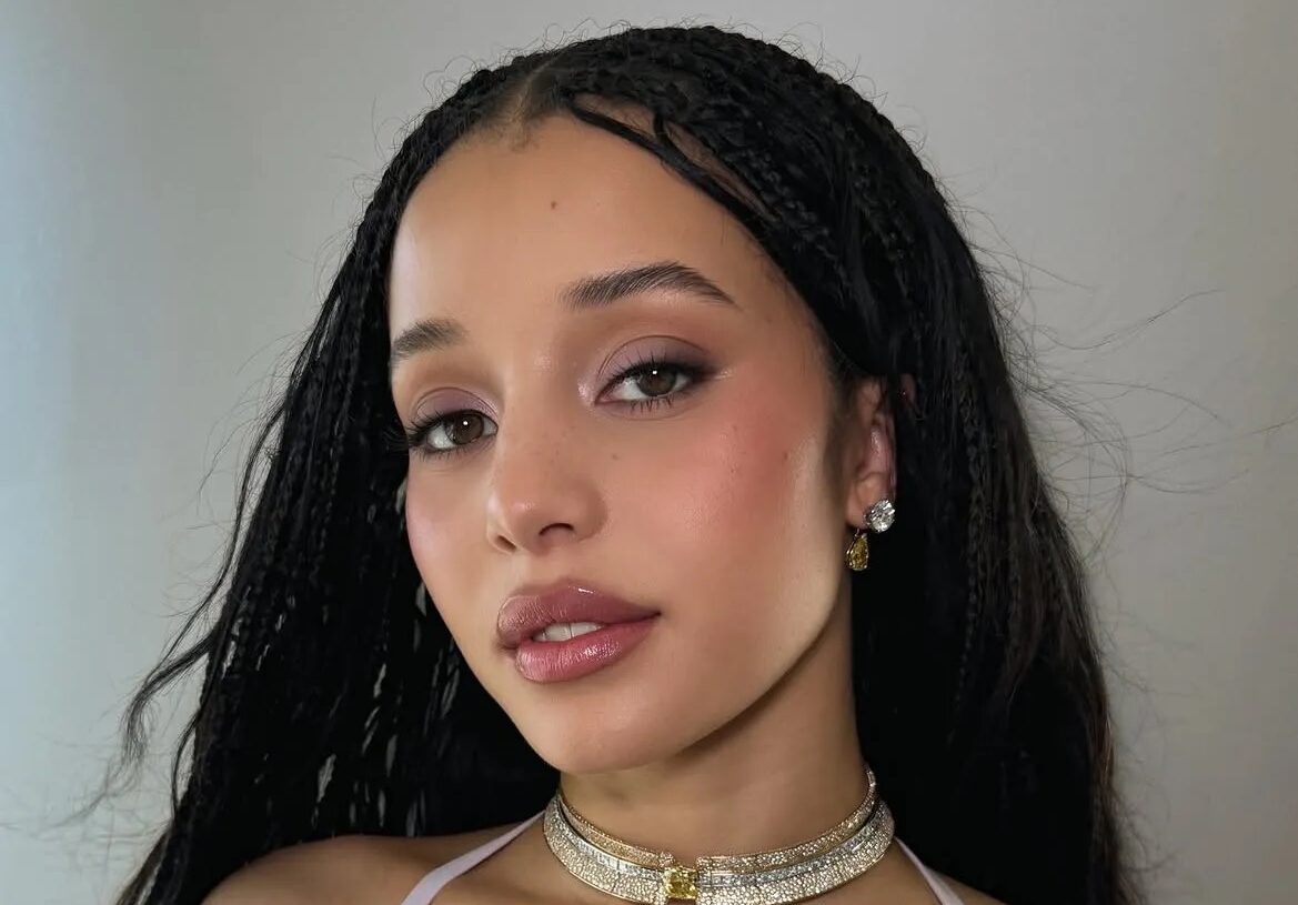 Chase Infiniti con trenzas oscuras, un vestido halter lila claro y un maquillaje sutil con sutiles acentos malva en los párpados.