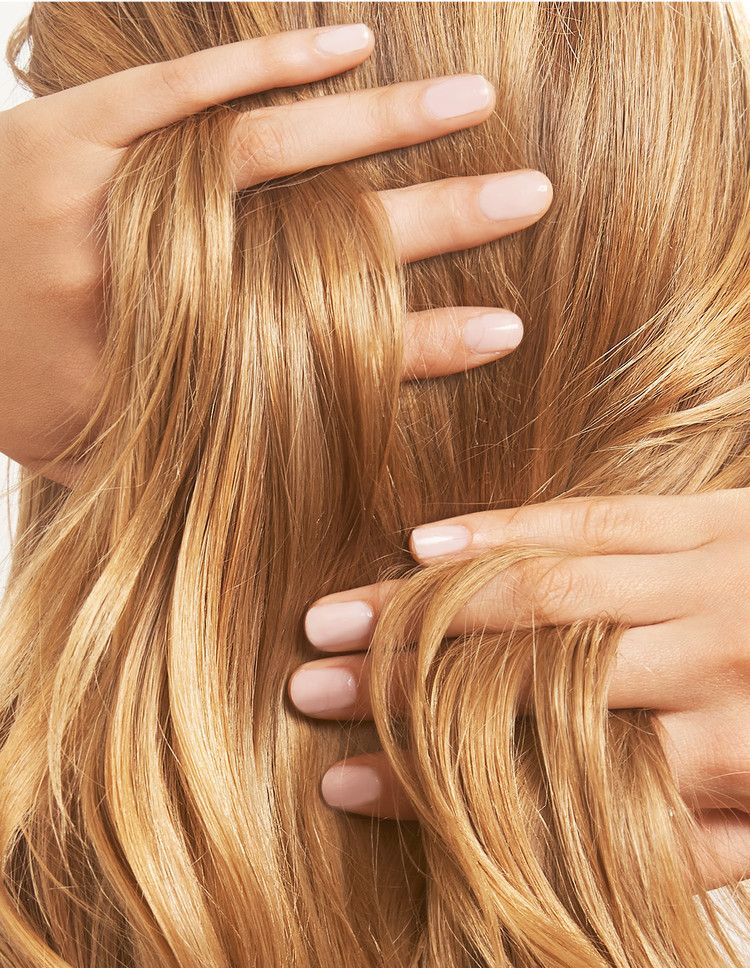 Manos con manicura en tono nude deslizándose a través de mechones de cabello rubio y luminoso
