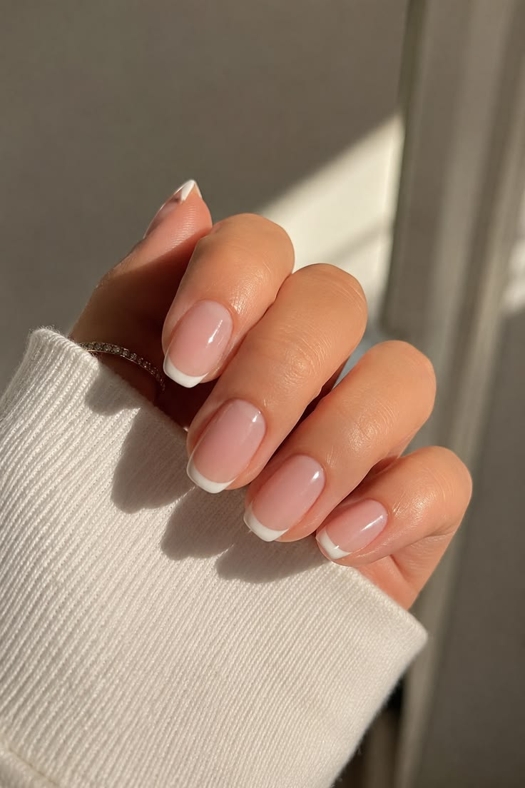 Mano con manicura francesa clásica de base rosada translúcida y líneas blancas definidas en las puntas, luciendo un anillo sutil.