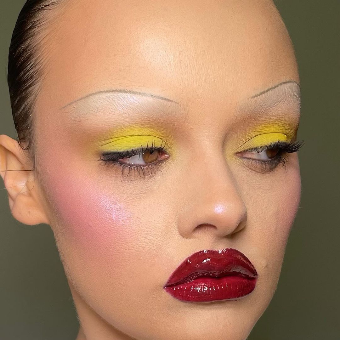 Maquillaje editorial con cejas finas pintadas.