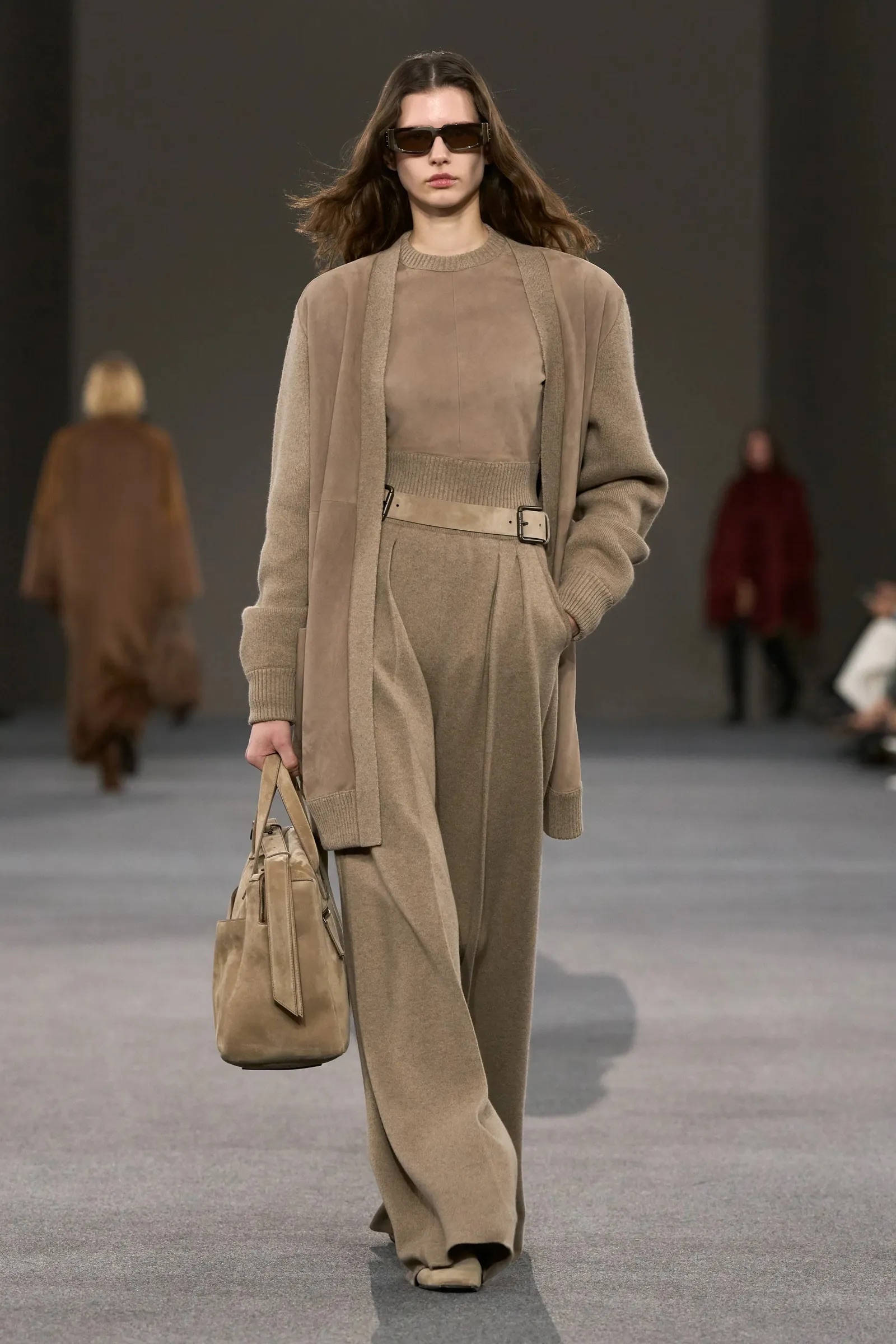 Modelo en tonos tierra con un cárdigan largo de ante, top a juego, pantalones anchos plisados con cinturón y un bolso de mano estructurado.