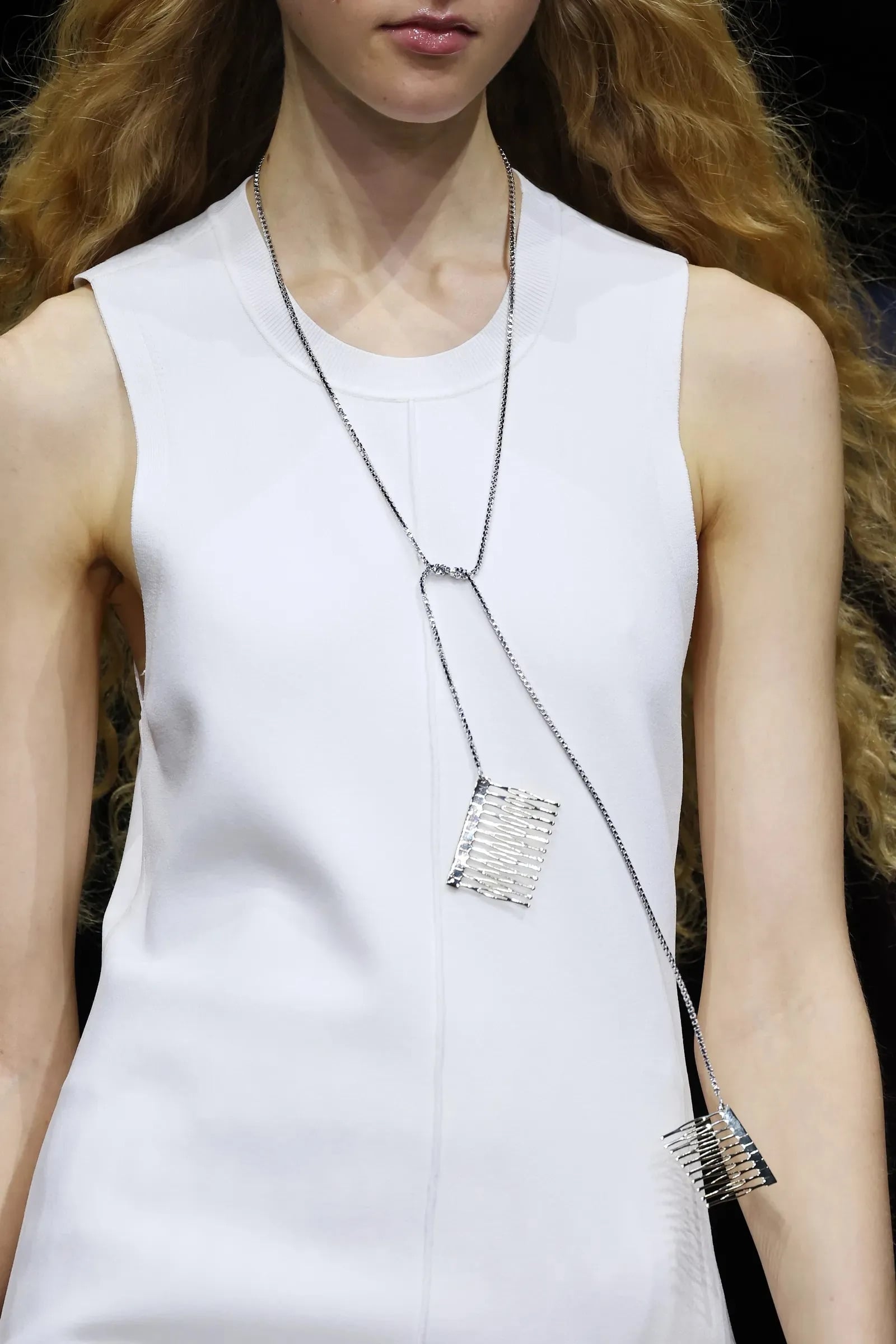 Modelo con blusa blanca sin mangas luciendo un collar largo de cadena fina con dijes metálicos dobles en forma de pequeñas peinetas.