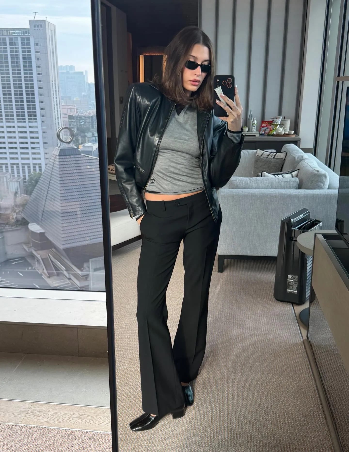 Mujer con chaqueta de cuero negra, top gris y pantalones negros minimalistas estilo años 90.