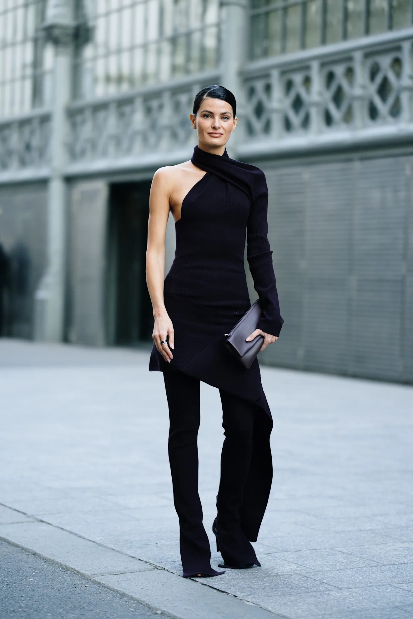 Mujer con vestido asimétrico oscuro y leggings o pantalones negros entallados en exteriores.