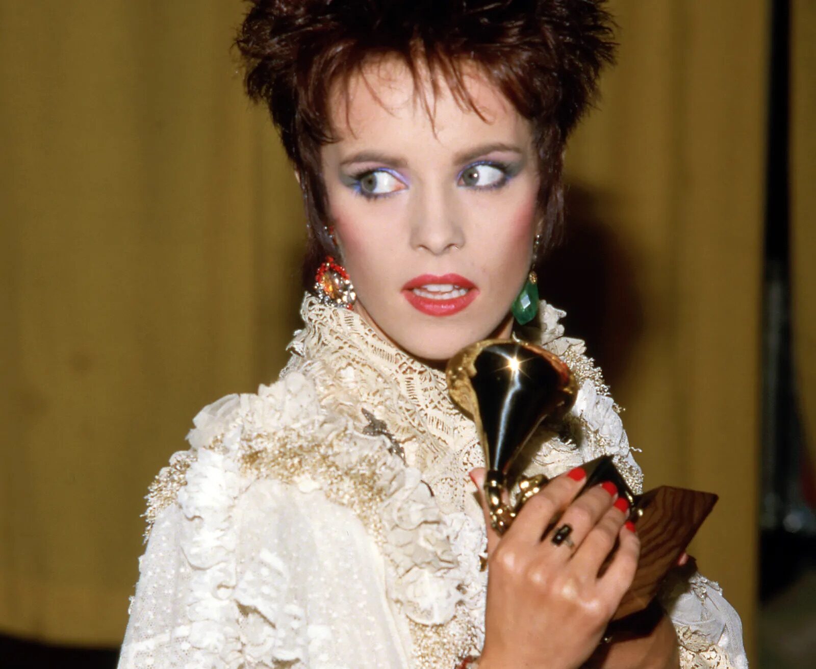 Sheena Easton luciendo una blusa de encaje blanco con volantes y pulseras llamativas mientras sostiene un premio Grammy en 1985.
