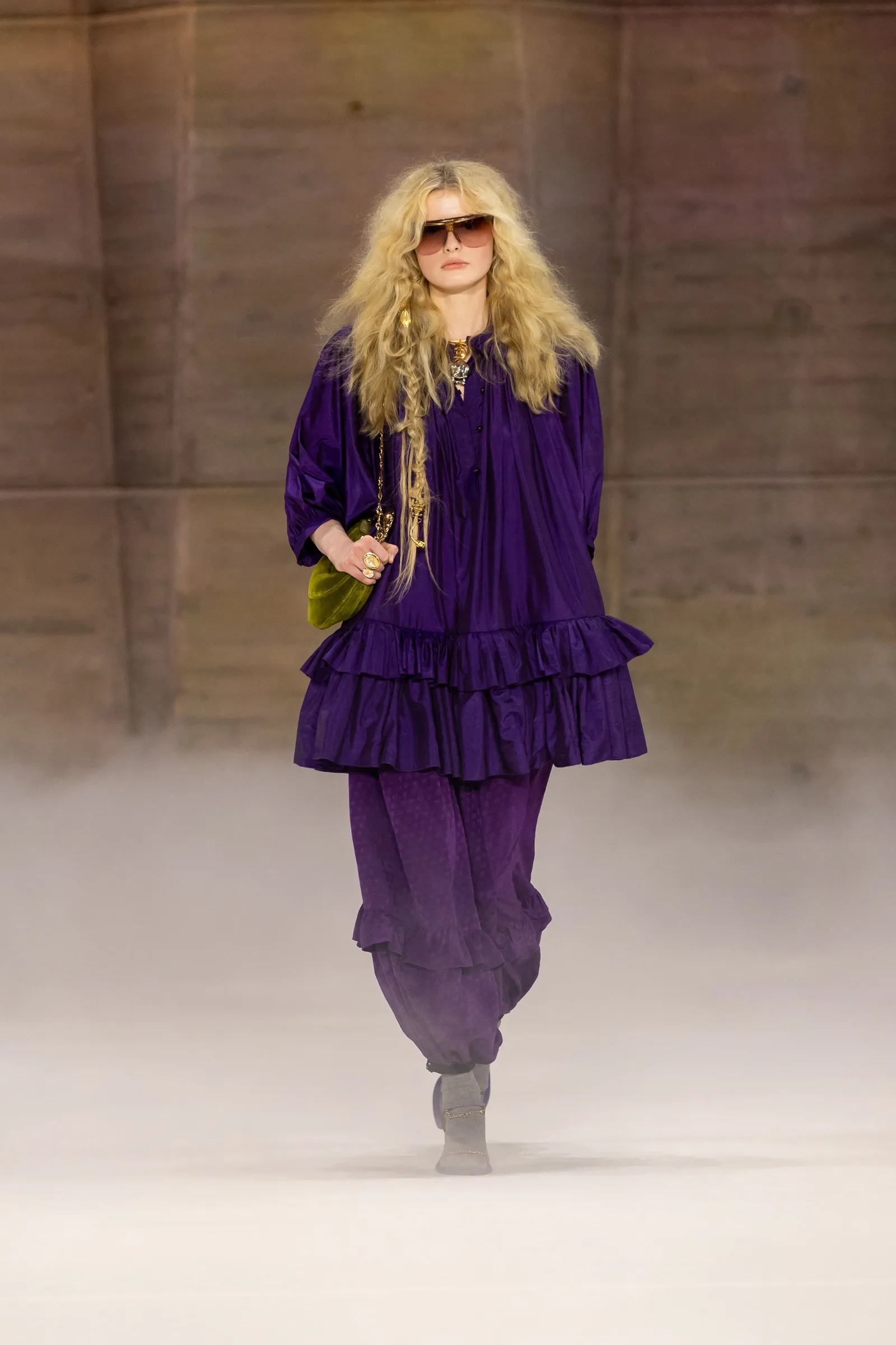 Modelo rubia con conjunto de blusa y pantalones en morado amatista caminando en pasarela.