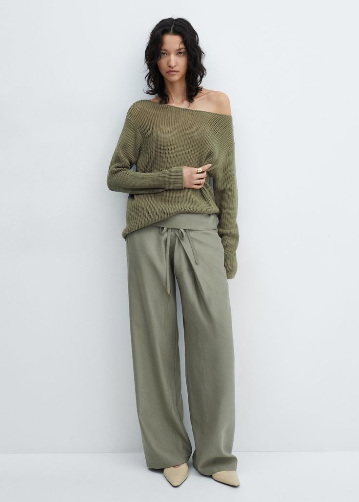 Modelo con un suéter de punto fino en tono verde oliva con escote de hombro caído y pantalones amplios a juego con cordón ajustable en la cintura.