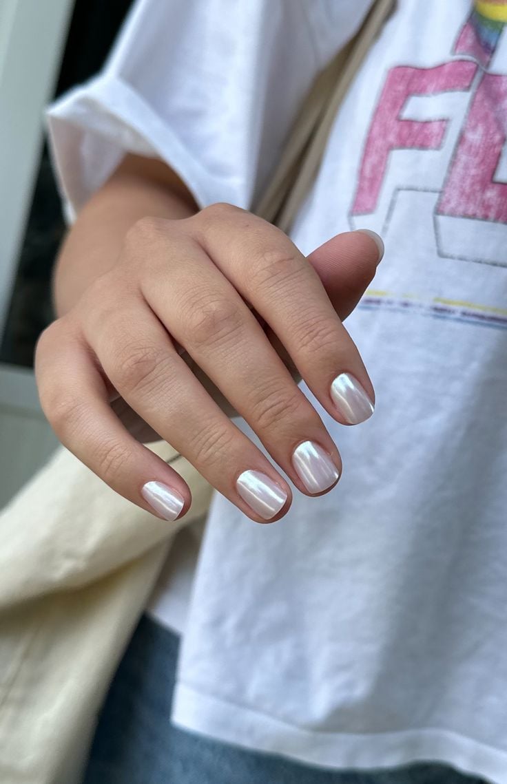 Mano con uñas cortas cuadradas con esquinas suavemente redondeadas y un acabado blanco cromado brillante que refleja la luz.