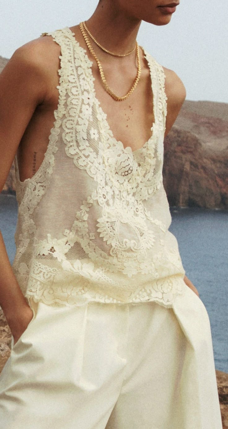 Camisola fluida de encaje en tono marfil con tirantes finos, combinada con pantalones claros y collares dorados.