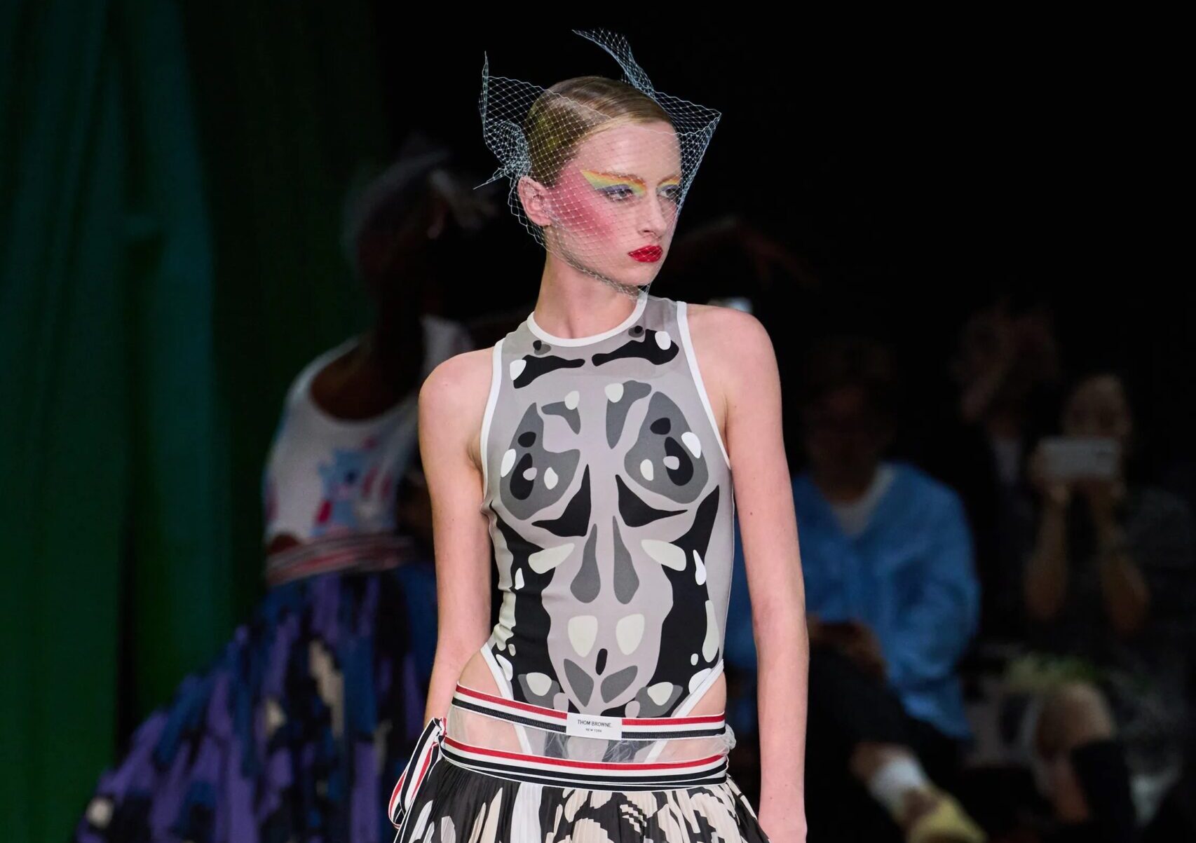 Modelo desfilando con un conjunto de inspiración entomológica, compuesto por un top ajustado sin mangas y una falda midi plisada con estampado de alas de mariposa en tonos grises, blancos y naranjas.